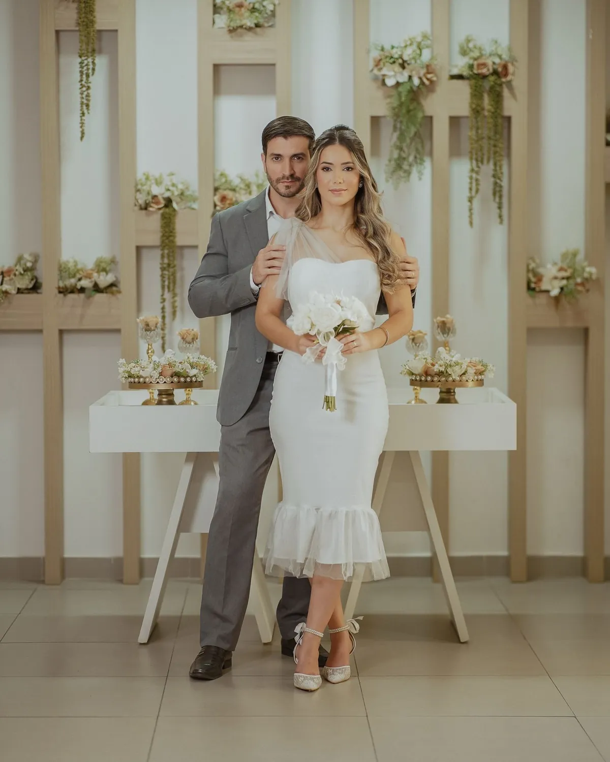 Casal de noivos no salão de casamentos do cartório, diante do painel de madeira com flores